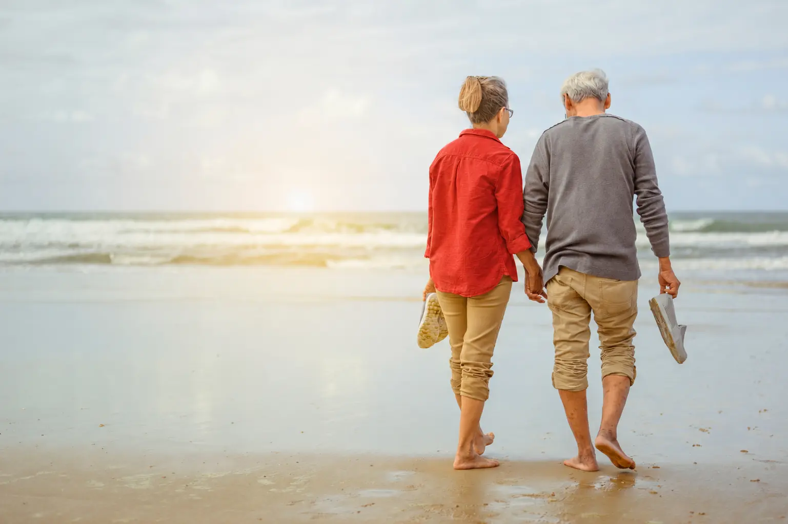 Pareja caminando de la mano por la playa, con una camisa roja como acento de color